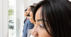 A diverse group of business professionals looking thoughtfully out of an office window.