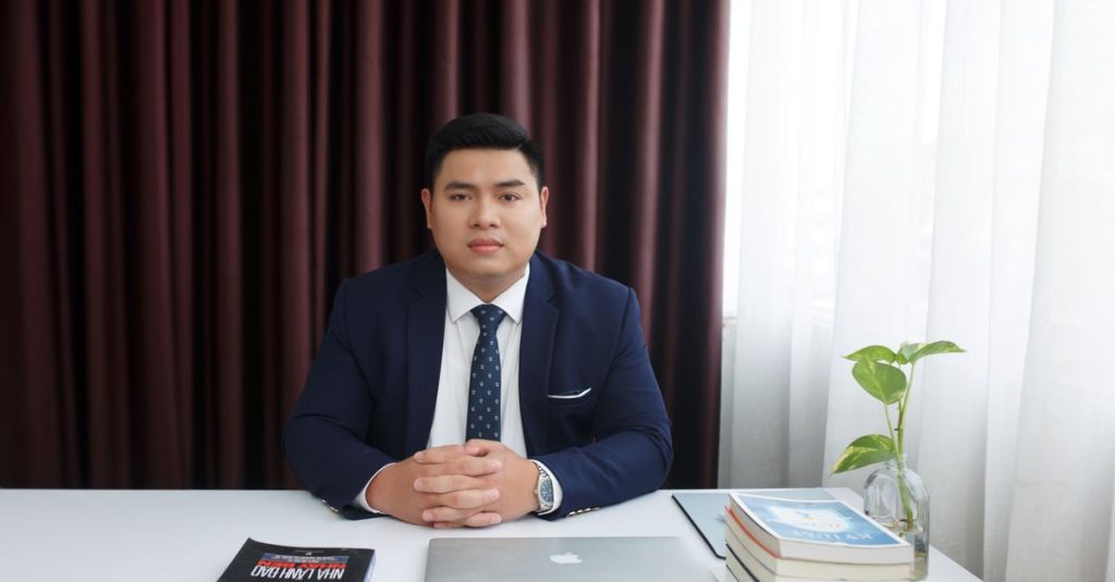 Người đàn ông mặc vest ngồi làm việc với máy tính xách tay và sách trong văn phòng.