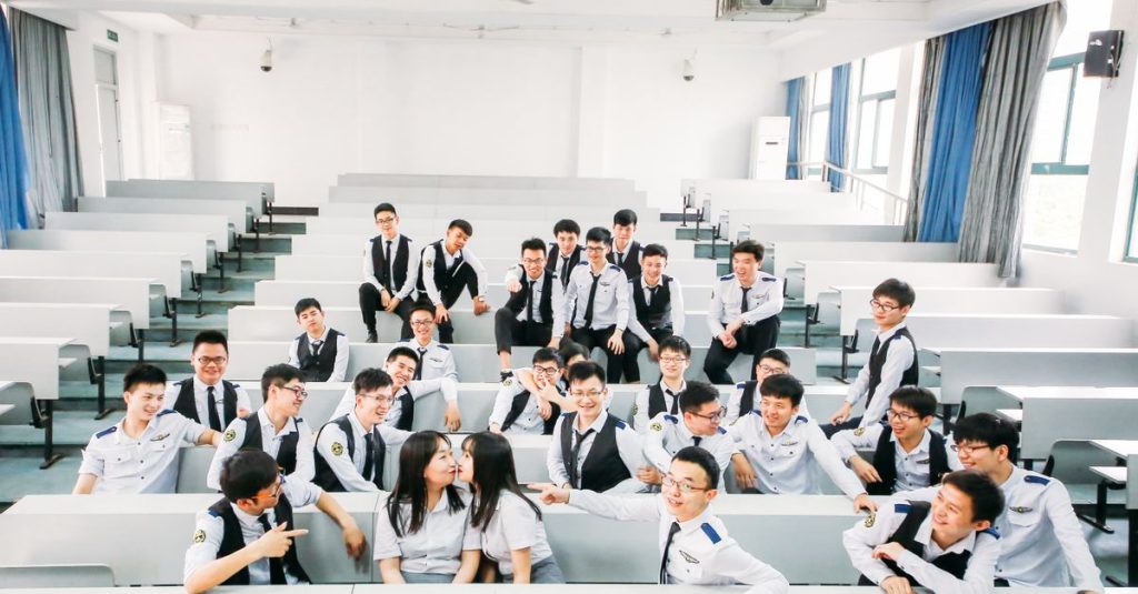 A lively group of college students in uniforms posing playfully in a classroom setting.