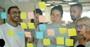 Diverse team strategizing with colorful sticky notes on glass wall in office.