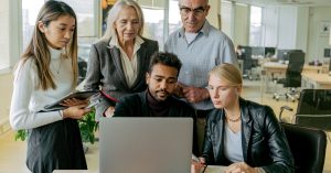 A diverse group of professionals collaborating around a laptop in a modern office setting.