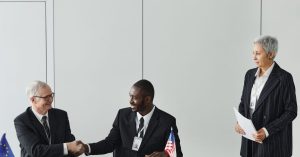 Multinational business meeting with agreement signing, featuring diverse professionals and flags.