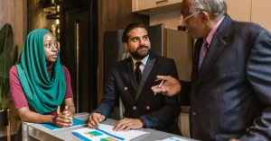 Three business professionals engage in a discussion, showcasing diversity and teamwork in a modern office setting.