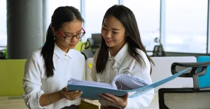 Two professional women reviewing documents together in a modern office setting, emphasizing teamwork.