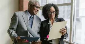 Two business professionals reviewing documents in a corporate office setting.
